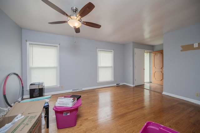 interior space featuring ceiling fan, visible vents, baseboards, and wood finished floors