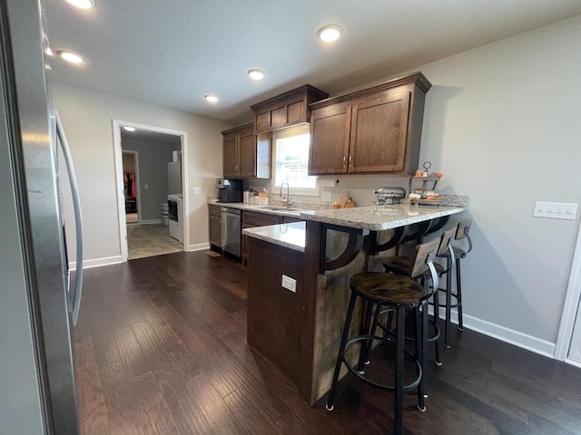 kitchen with a sink, a breakfast bar area, stainless steel appliances, a peninsula, and dark wood-style floors