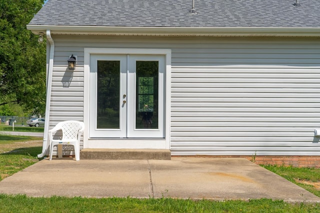 view of exterior entry featuring a shingled roof, a patio area, and french doors