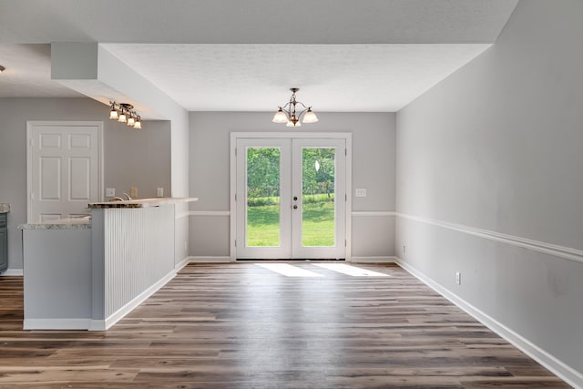 unfurnished dining area featuring baseboards, french doors, wood finished floors, and a chandelier