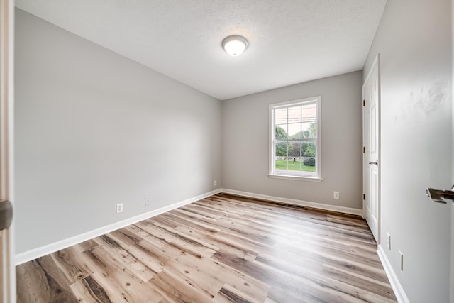 spare room featuring light wood-style floors, baseboards, a textured ceiling, and visible vents