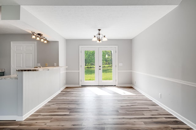 unfurnished dining area with an inviting chandelier, baseboards, french doors, and wood finished floors