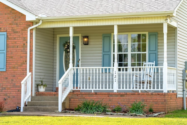 property entrance featuring roof with shingles, a porch, and brick siding