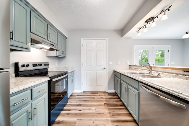 kitchen with a textured ceiling, under cabinet range hood, a sink, light wood-style flooring, and appliances with stainless steel finishes