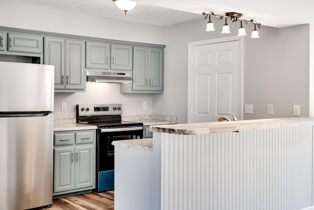 kitchen with a peninsula, light countertops, under cabinet range hood, light wood finished floors, and appliances with stainless steel finishes
