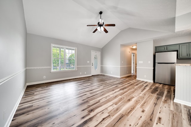 unfurnished living room featuring ceiling fan, vaulted ceiling, baseboards, and light wood-type flooring