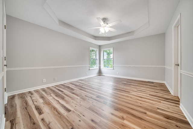 empty room featuring a raised ceiling, baseboards, a ceiling fan, and light wood-type flooring