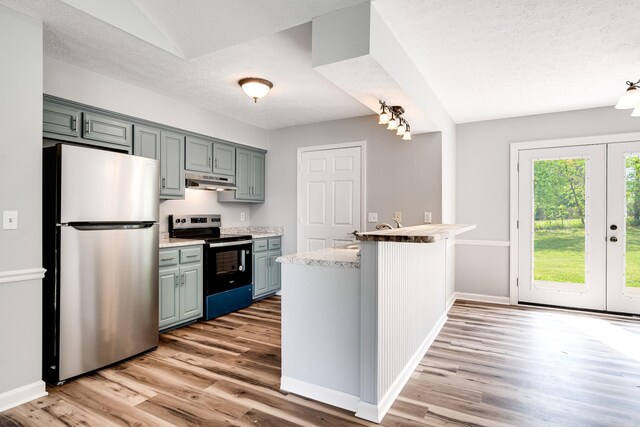 kitchen featuring a peninsula, light wood-style floors, a textured ceiling, under cabinet range hood, and stainless steel appliances