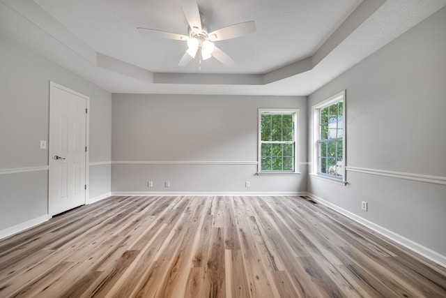empty room with ceiling fan, baseboards, wood finished floors, a tray ceiling, and visible vents