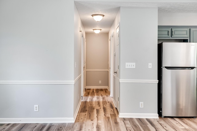 hall with a textured ceiling, baseboards, and light wood finished floors