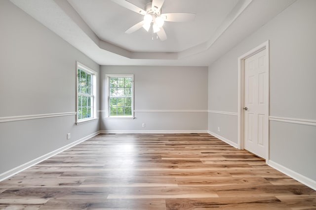 spare room featuring baseboards, a raised ceiling, ceiling fan, and wood finished floors
