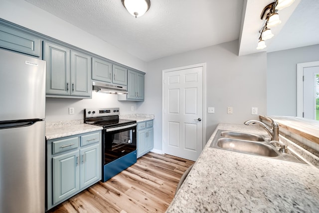 kitchen featuring a sink, light wood finished floors, stainless steel appliances, under cabinet range hood, and blue cabinets