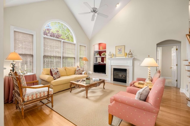 living area featuring built in features, high vaulted ceiling, a ceiling fan, and light wood-style flooring
