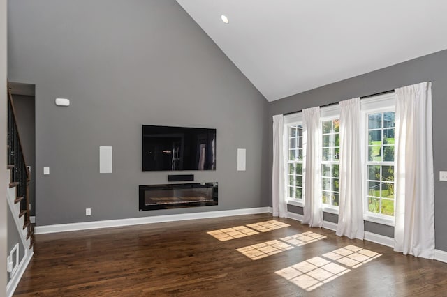 unfurnished living room with baseboards, high vaulted ceiling, a healthy amount of sunlight, and stairway