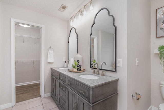 bathroom featuring a walk in closet, a sink, double vanity, toilet, and visible vents