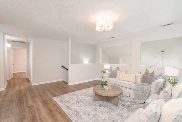 living room featuring visible vents, a textured ceiling, baseboards, and wood finished floors