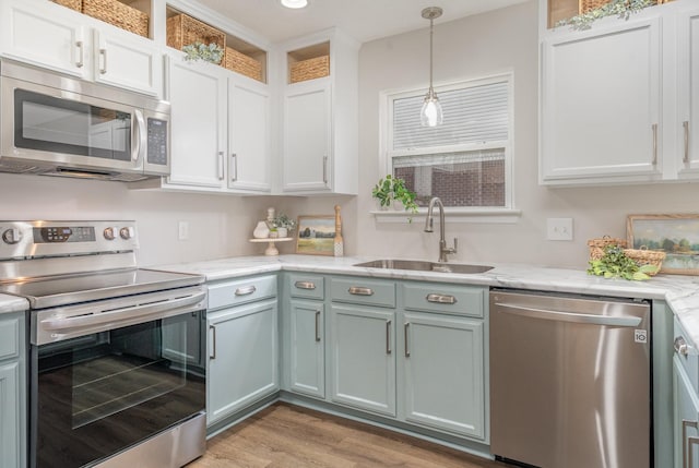 kitchen with hanging light fixtures, a sink, light wood finished floors, stainless steel appliances, and white cabinetry