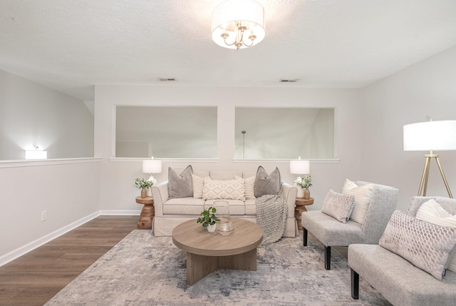 living area with a textured ceiling, baseboards, visible vents, and wood finished floors