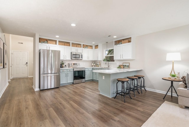 kitchen featuring appliances with stainless steel finishes, a sink, a peninsula, baseboards, and a kitchen bar