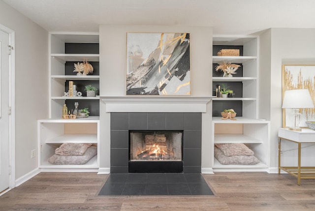 interior details featuring built in shelves, a tile fireplace, and wood finished floors