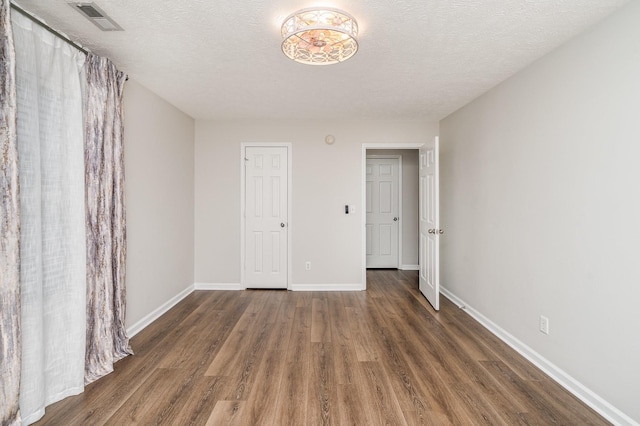 spare room featuring visible vents, a textured ceiling, baseboards, and wood finished floors