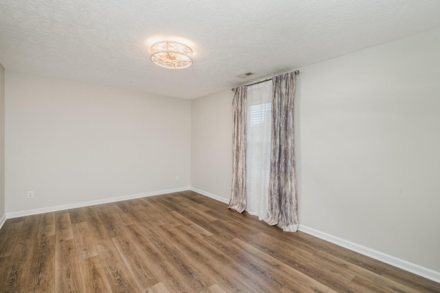 empty room featuring baseboards, a textured ceiling, wood finished floors, and visible vents