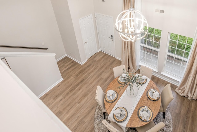 dining room featuring visible vents, a towering ceiling, wood finished floors, baseboards, and a notable chandelier