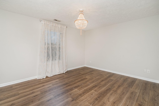 spare room with visible vents, an inviting chandelier, wood finished floors, baseboards, and a textured ceiling
