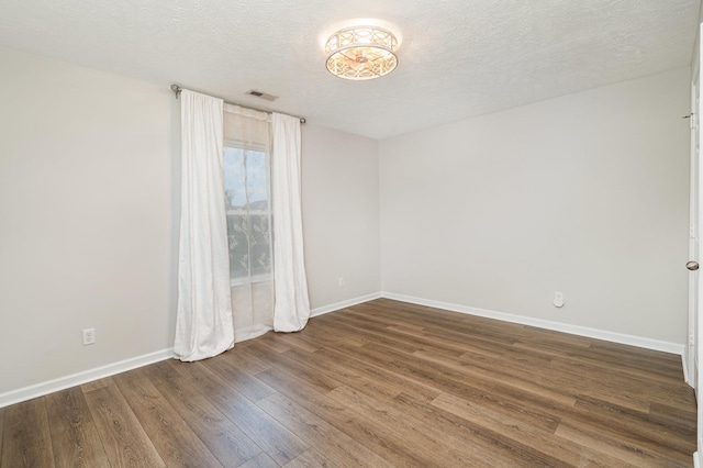 unfurnished room featuring baseboards, a textured ceiling, wood finished floors, and visible vents