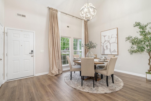dining room featuring an inviting chandelier, a towering ceiling, wood finished floors, and visible vents