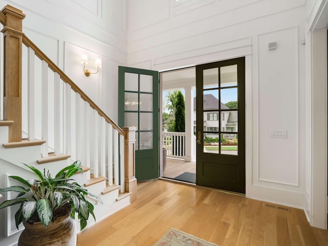 foyer entrance with a decorative wall, stairs, wood finished floors, and visible vents
