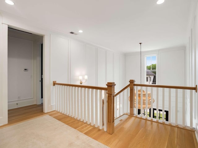 corridor with visible vents, light wood finished floors, an upstairs landing, a decorative wall, and recessed lighting