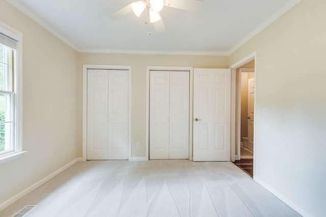 unfurnished bedroom featuring multiple closets, multiple windows, light carpet, and visible vents