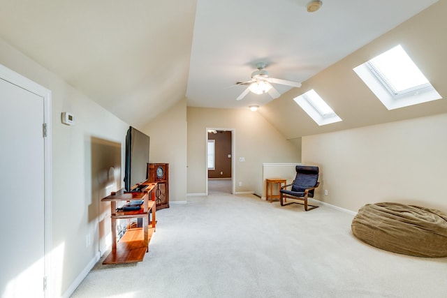 living area with light colored carpet, a ceiling fan, baseboards, and vaulted ceiling with skylight