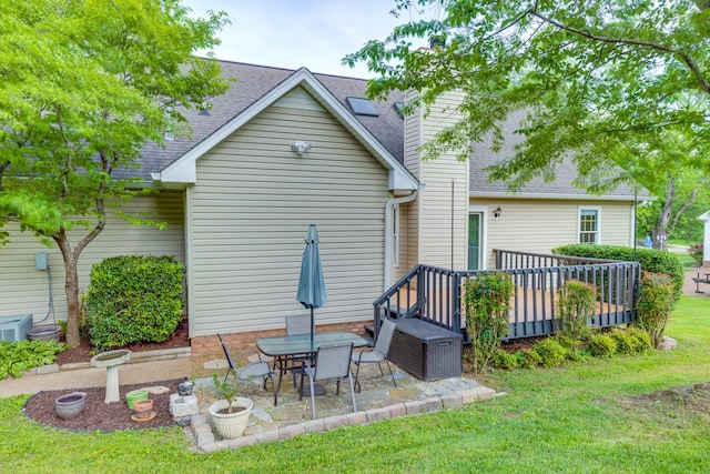 rear view of property with a chimney, roof with shingles, a wooden deck, a patio area, and a yard