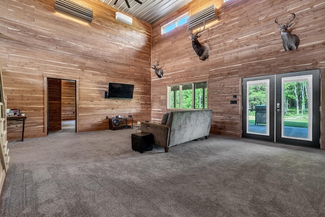 carpeted living area featuring wooden walls, a healthy amount of sunlight, french doors, and a towering ceiling