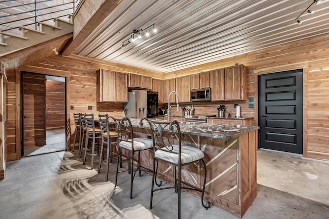 kitchen with unfinished concrete floors, stainless steel appliances, and wooden walls