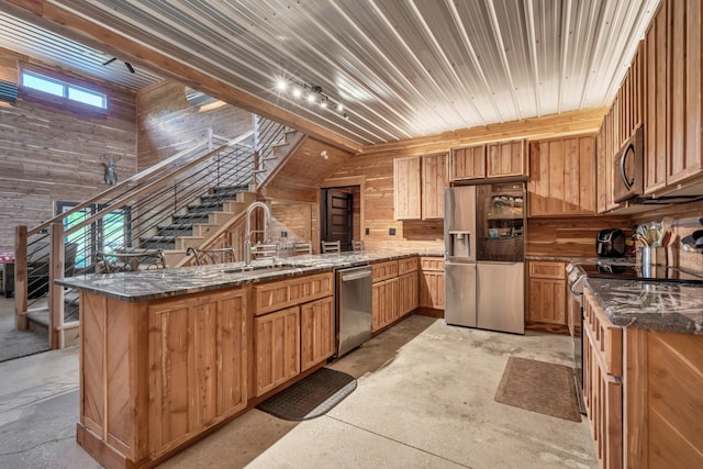 kitchen featuring wood walls, appliances with stainless steel finishes, concrete floors, and a sink