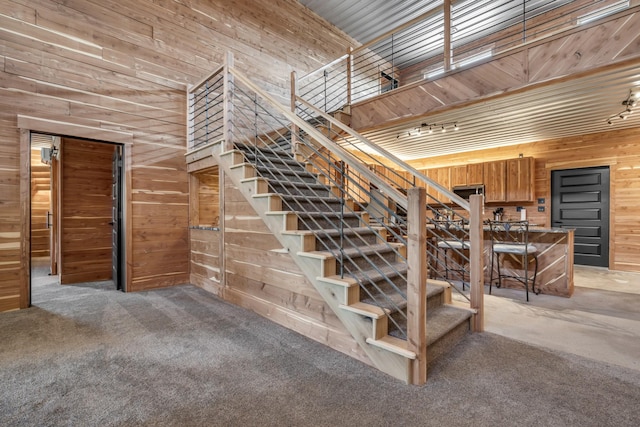 staircase with carpet flooring, a high ceiling, and wood walls