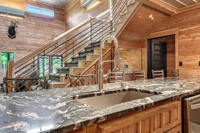 kitchen with wooden walls, wood ceiling, dark stone countertops, and a sink