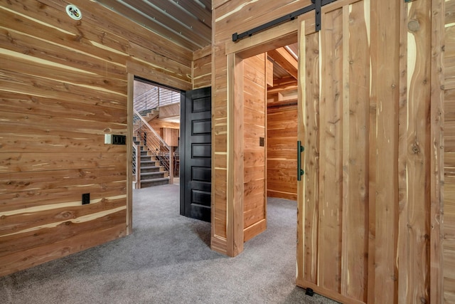 interior space with a barn door, wooden walls, stairway, and carpet flooring