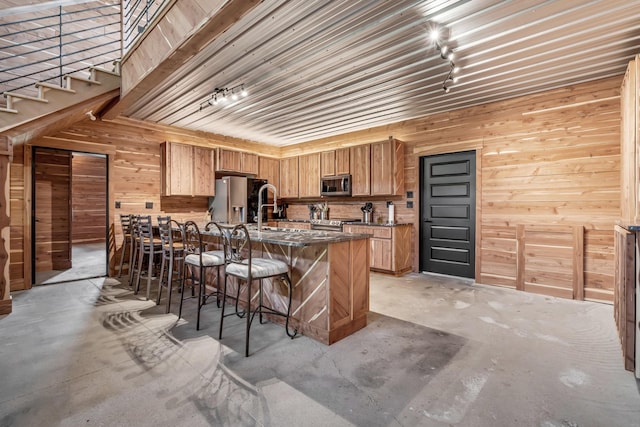 kitchen featuring wood walls, a peninsula, a kitchen breakfast bar, concrete floors, and appliances with stainless steel finishes