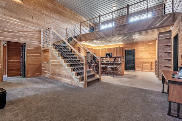 stairs with wooden walls, a high ceiling, and carpet flooring
