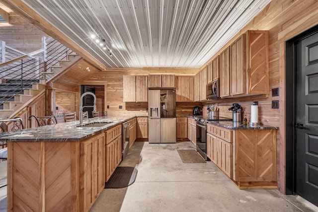 kitchen with a peninsula, dark stone counters, a sink, concrete floors, and appliances with stainless steel finishes