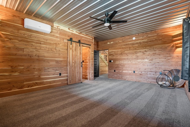 carpeted spare room with wooden walls, a ceiling fan, a wall mounted AC, and a barn door