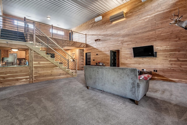 carpeted living room with wooden walls, stairway, and a towering ceiling