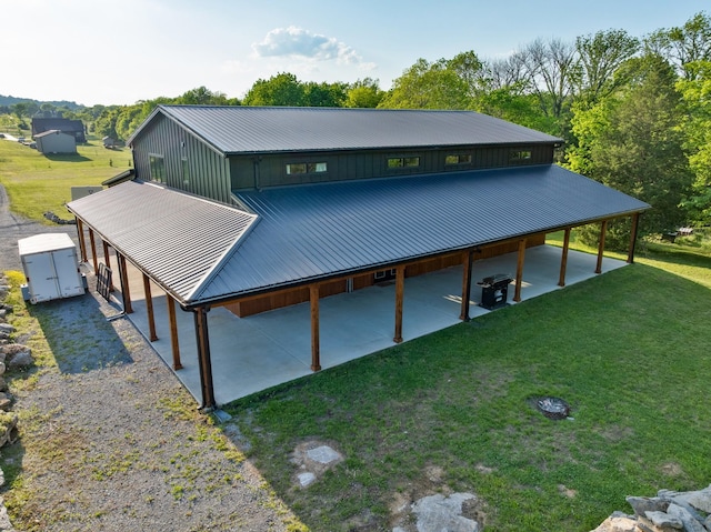 back of property with an outdoor structure, a shed, a patio area, metal roof, and a lawn