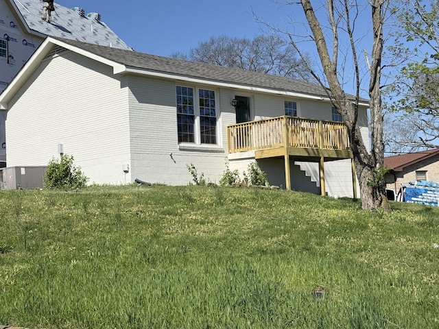 back of property featuring a lawn, central AC unit, roof with shingles, and a deck