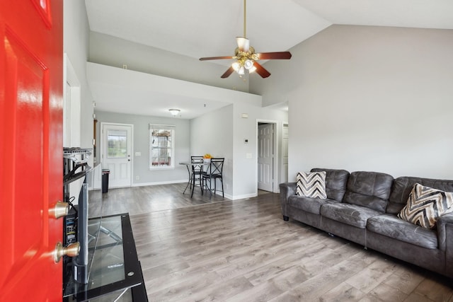 living area with baseboards, a ceiling fan, wood finished floors, and high vaulted ceiling