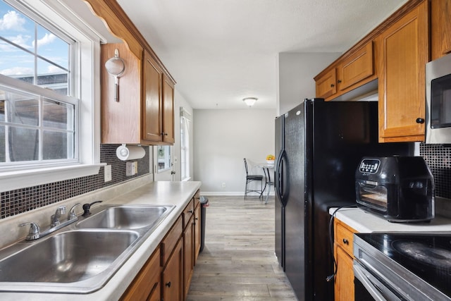kitchen featuring a sink, light wood finished floors, brown cabinetry, decorative backsplash, and a wealth of natural light